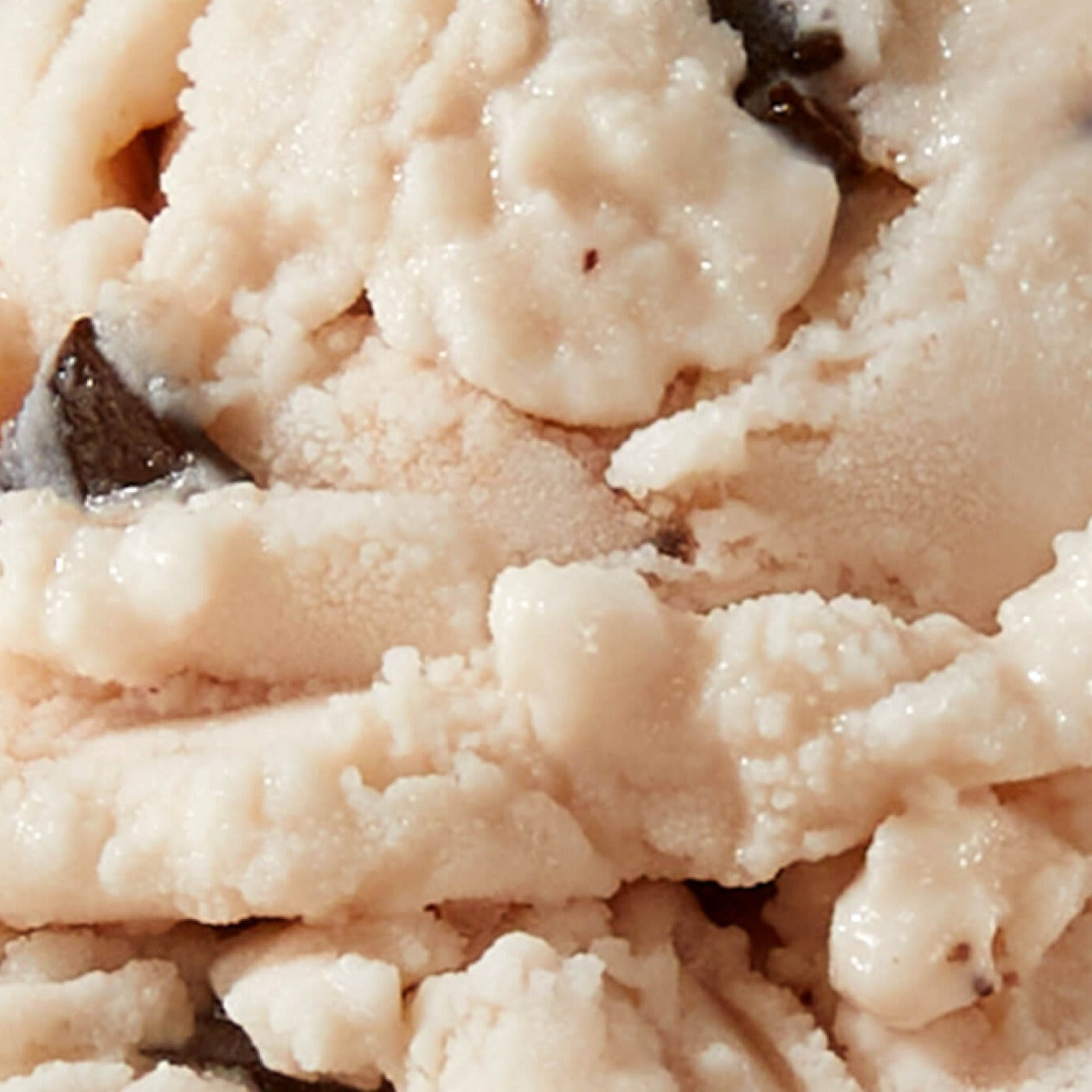 Extreme close-up texture shot of N!CK'S Cherry Chocolate light ice cream, showing light-colored ice cream with specks of dark chocolate and swirls of cherry.