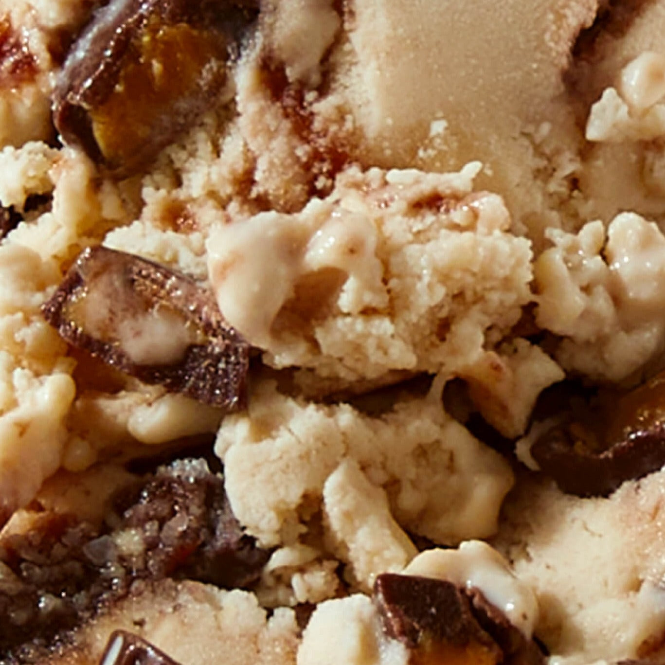 Extreme close-up texture shot of N!CK'S Peanut Butter Cup light ice cream, showing swirls of peanut butter ice cream with chunks of chocolate and peanut butter cup candy pieces.