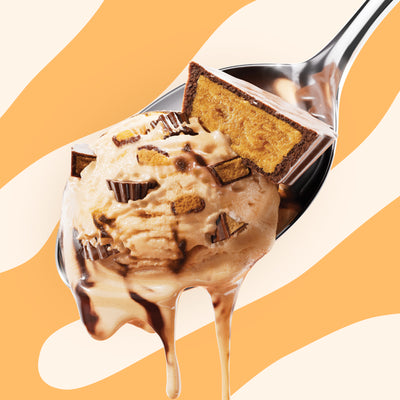 Pint of N!CK'S Peanut Butter Cup light ice cream. The label highlights 'no added sugar' and '390 calories/pint'. A spoon holds a scoop of peanut butter ice cream with visible peanut butter cup pieces and fudge swirl.