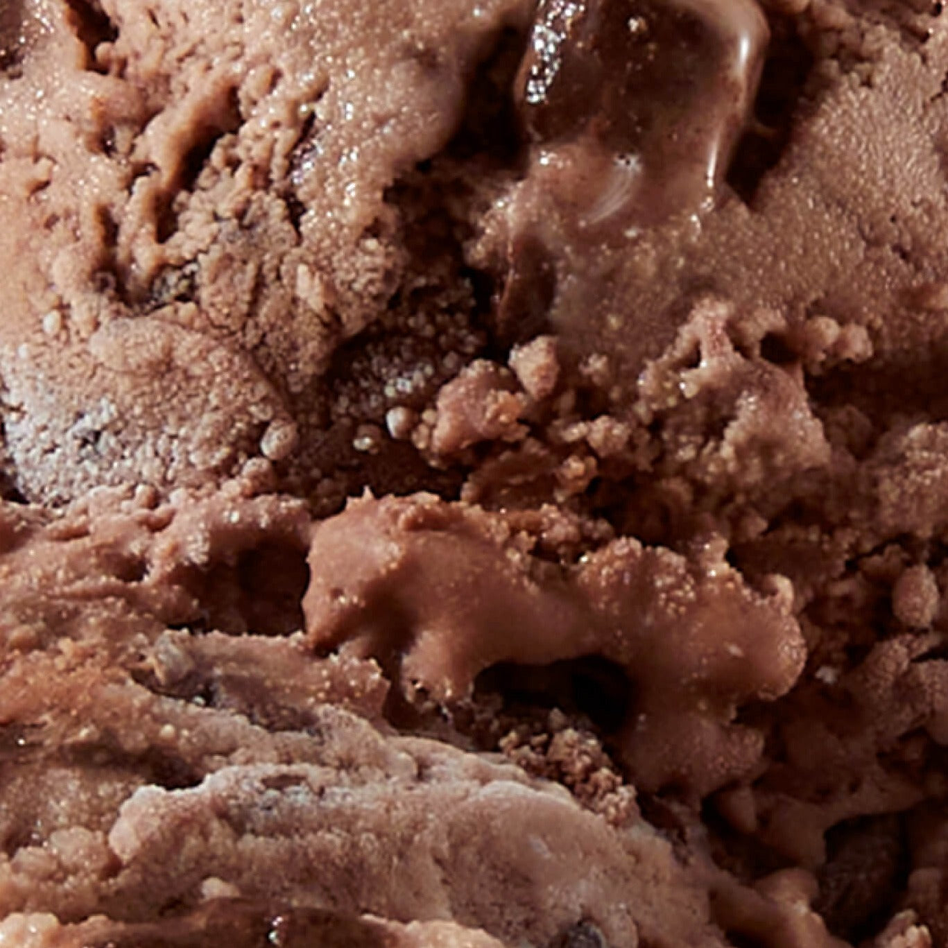 Extreme close-up texture shot of N!CK'S Triple Chocolate Brownie light ice cream, showing rich chocolate ice cream mixed with dark chocolate pieces and a moist, fudge-like texture.