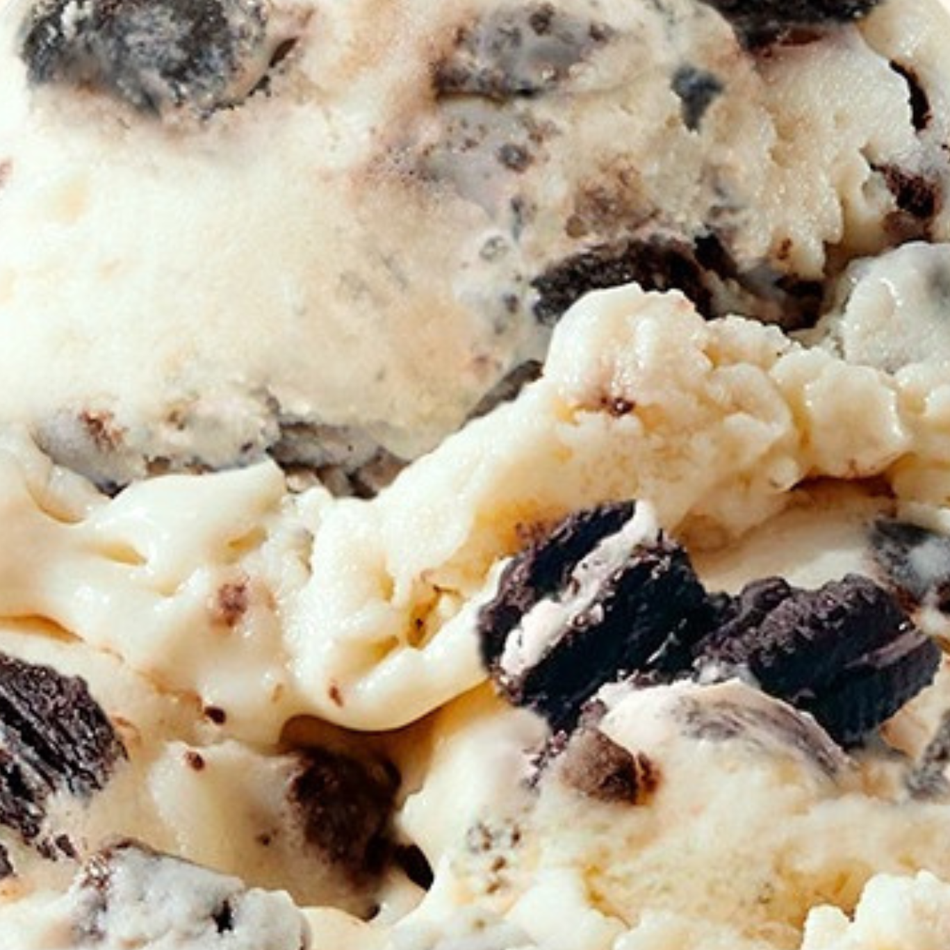 Extreme close-up texture shot of N!CK'S Cookies & Cream light ice cream, showing white vanilla ice cream with chunks of dark chocolate sandwich cookie pieces.