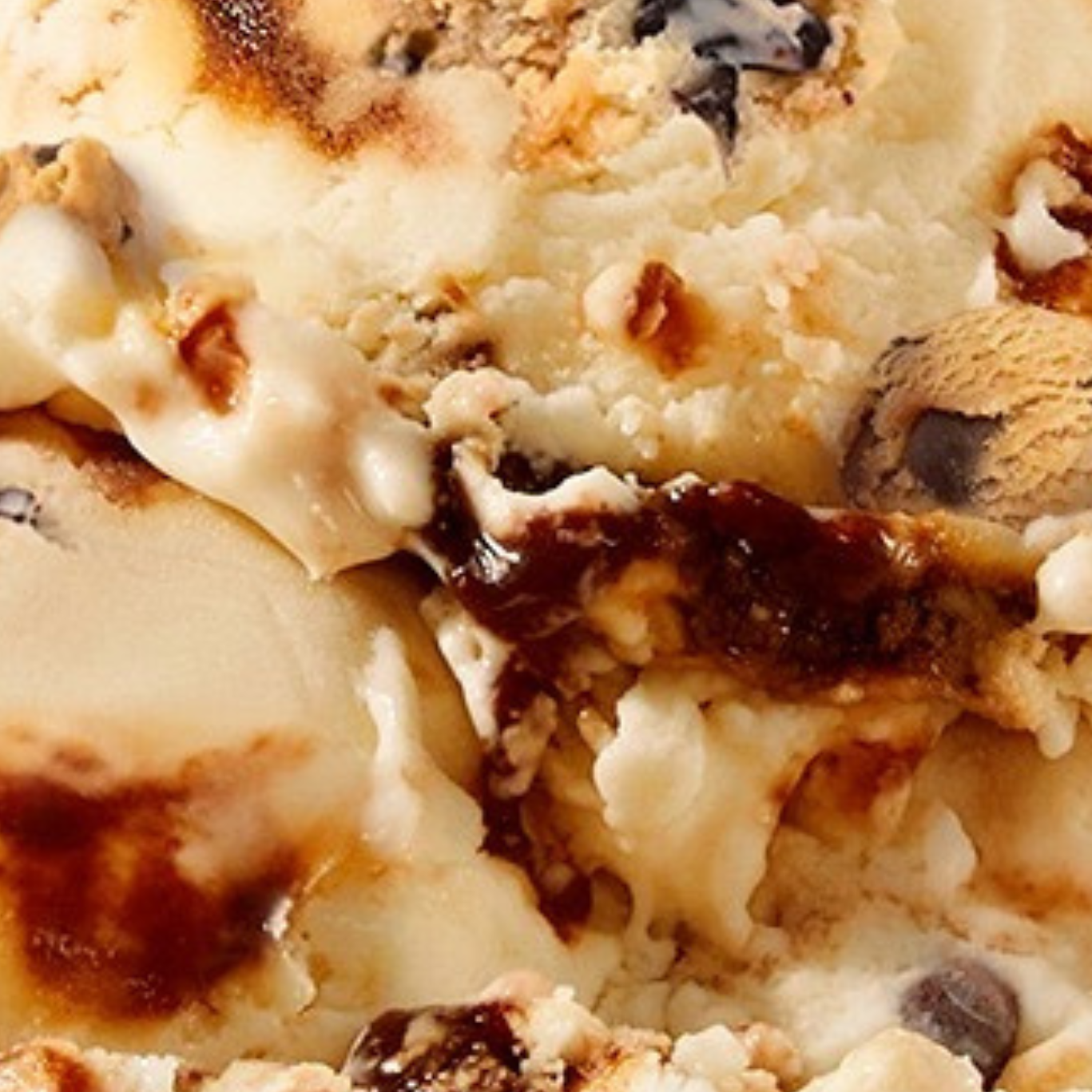 Extreme close-up texture shot of N!CK'S Chocolate Chip Cookie Dough light ice cream, showing vanilla ice cream with fudge swirls and visible chocolate chips and cookie dough chunks.